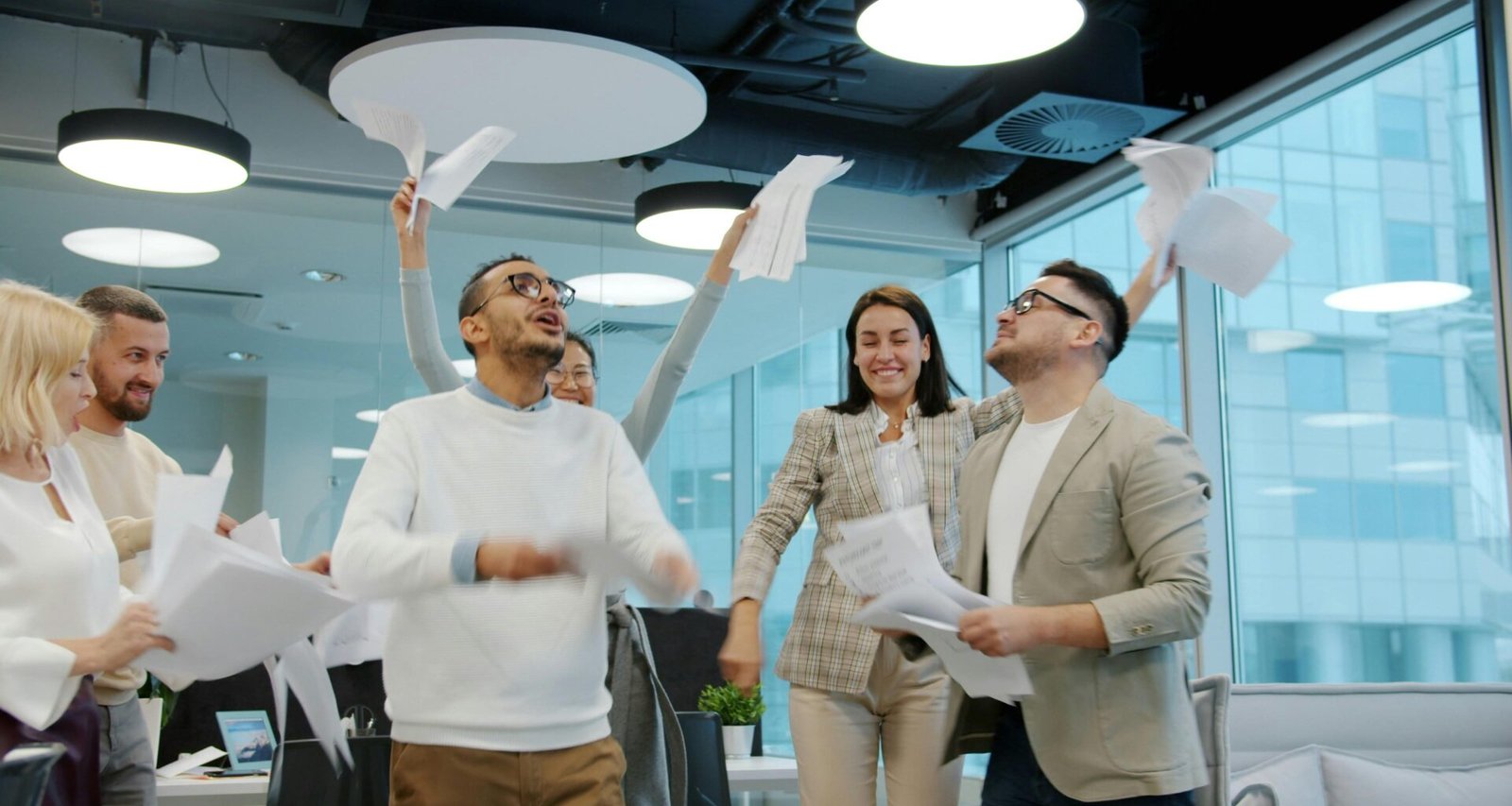 Diverse Gruppe von Kollegen wirft Papier in die Luft und feiert einen Projekterfolg im modernen Büro