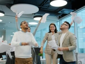 Diverse Gruppe von Kollegen wirft Papier in die Luft und feiert einen Projekterfolg im modernen Büro