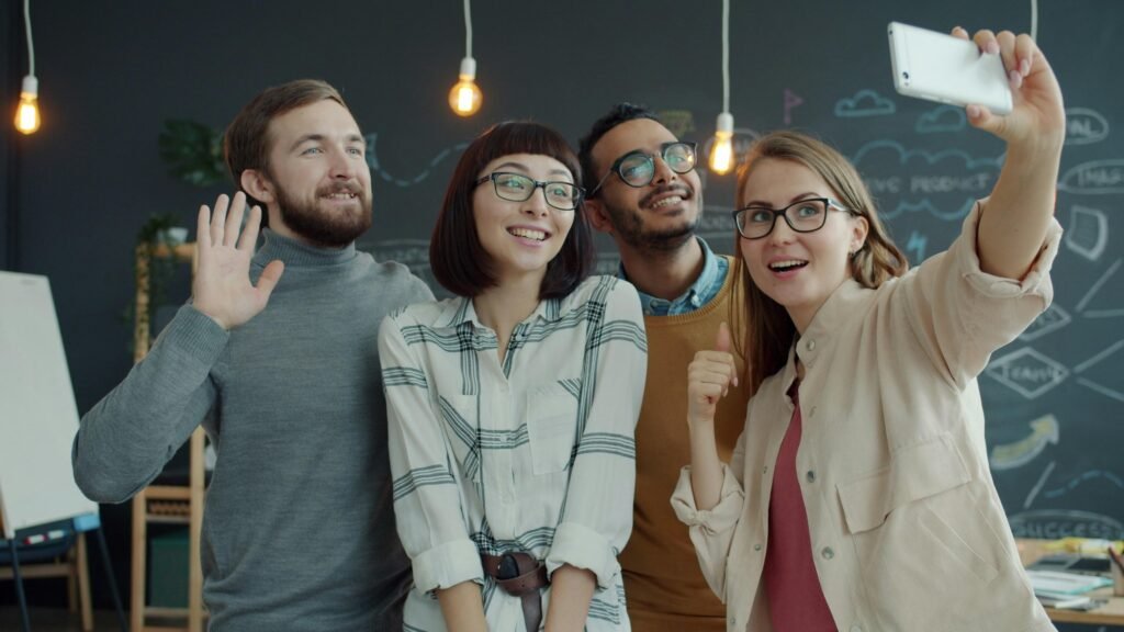 Vier junge Erwachsene machen gemeinsam ein Selfie in einem offenen, modernen Büro mit freundlicher Atmosphäre