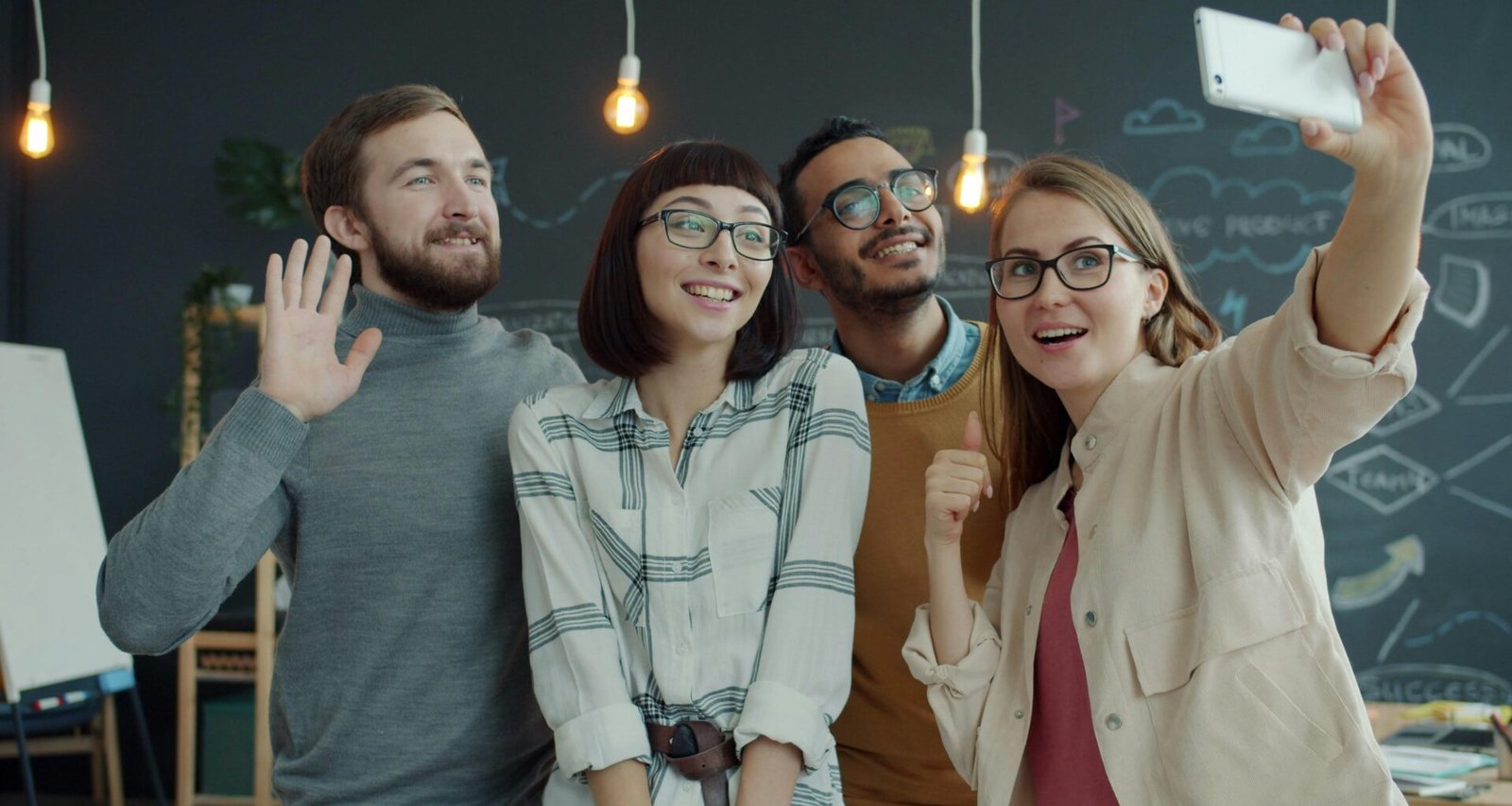 Vier junge Erwachsene machen gemeinsam ein Selfie in einem offenen, modernen Büro mit freundlicher Atmosphäre