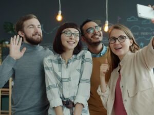 Vier junge Erwachsene machen gemeinsam ein Selfie in einem offenen, modernen Büro mit freundlicher Atmosphäre