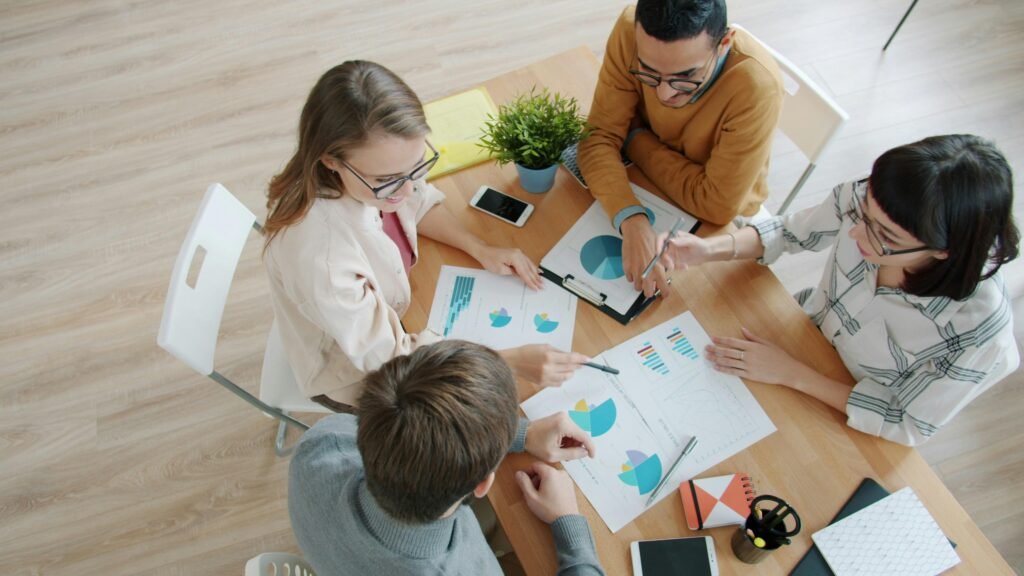 Vier Personen sitzen um einen Tisch und besprechen gemeinsam verschiedene Diagramme und Auswertungen.
