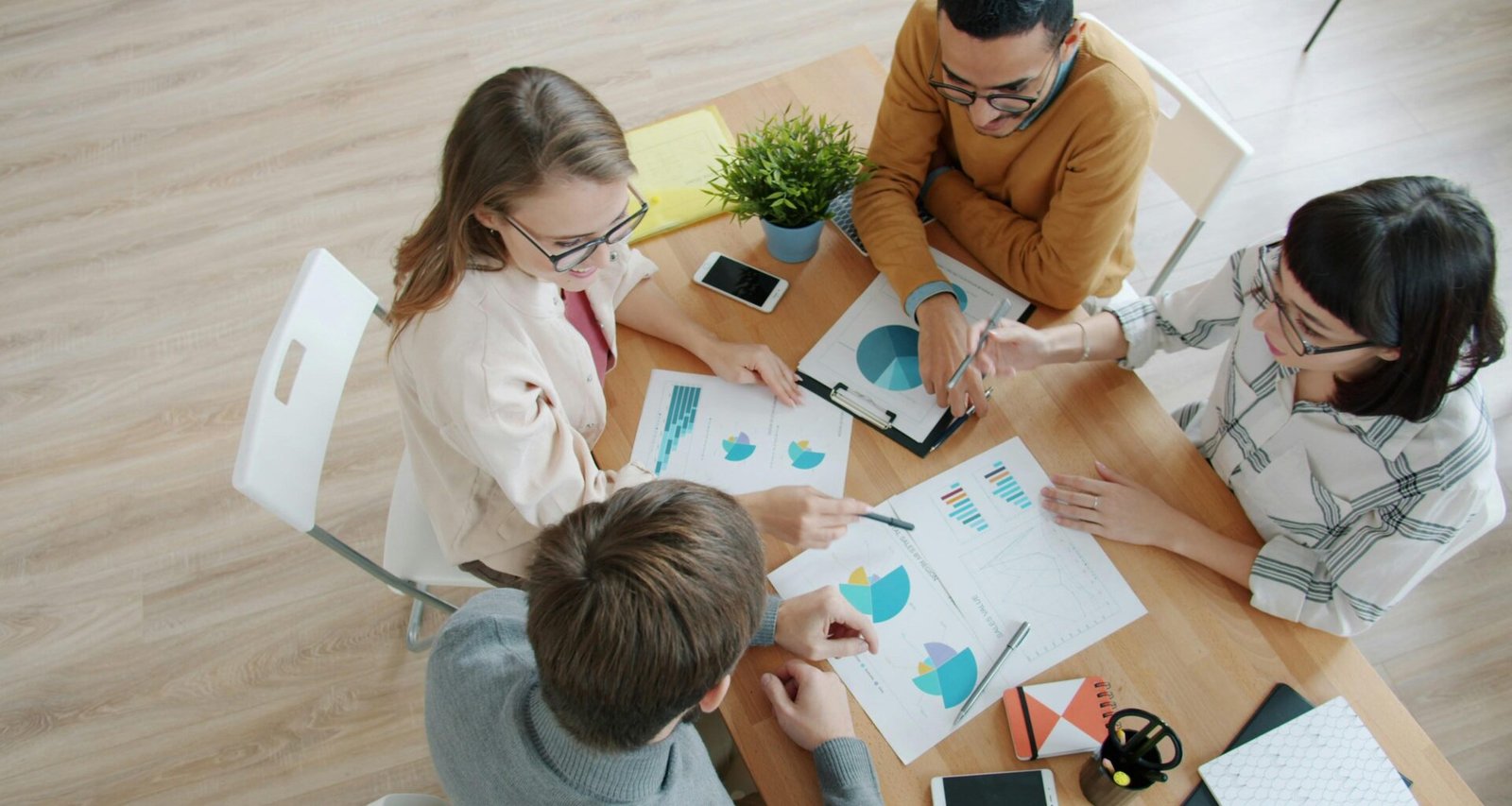 Vier Personen sitzen um einen Tisch und besprechen gemeinsam verschiedene Diagramme und Auswertungen.
