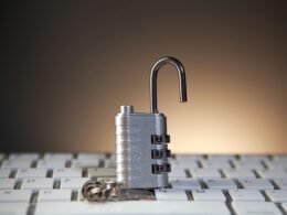 Offenes Zahlenschloss mit Zahlenkombination liegt auf schwarzer Computertastatur und symbolisiert Datensicherheit.
