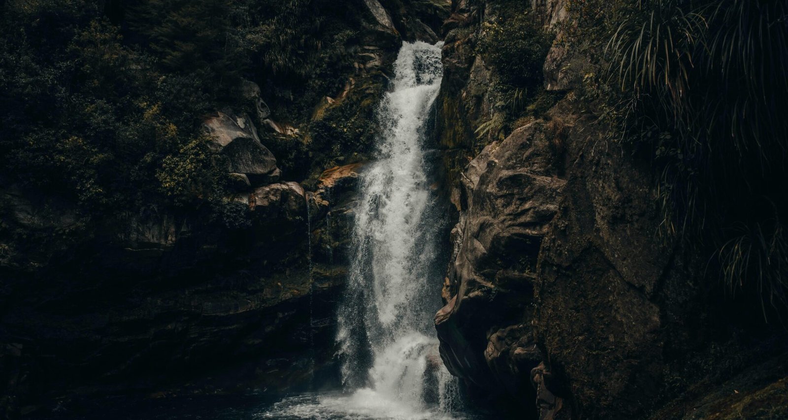Mehrere Wasserfälle fließen bei Tageslicht durch eine braune, felsige Berglandschaft mit steinigem Untergrund
