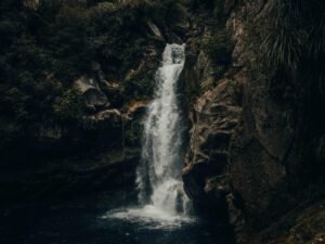 Mehrere Wasserfälle fließen tagsüber über braune, felsige Berghänge, umgeben von natürlicher Vegetation.