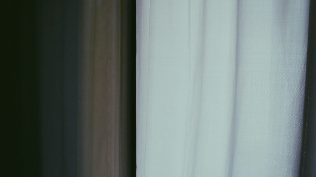 Weiße, halbtransparente Vorhänge lassen natürliches Licht in einen ruhigen, hellen Raum strömen