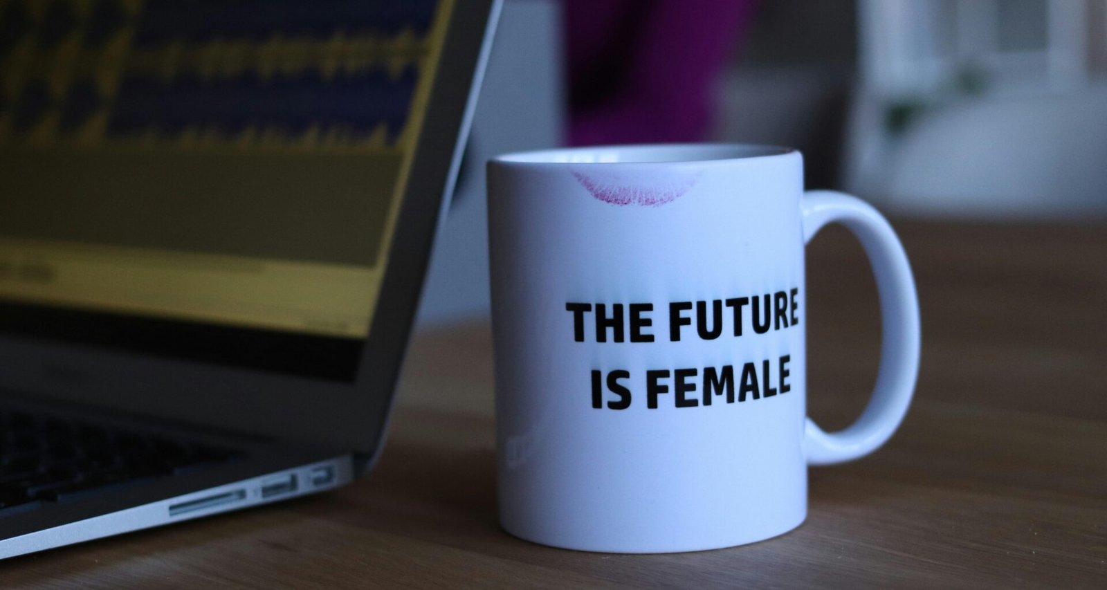 Schwarz-weiß bedruckte Keramiktasse steht neben einem aufgeklappten Laptop auf einem modernen Schreibtisch.