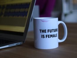 Weiße und schwarze bedruckte Keramiktasse neben einem Laptop auf einem Schreibtisch in einer Büroumgebung