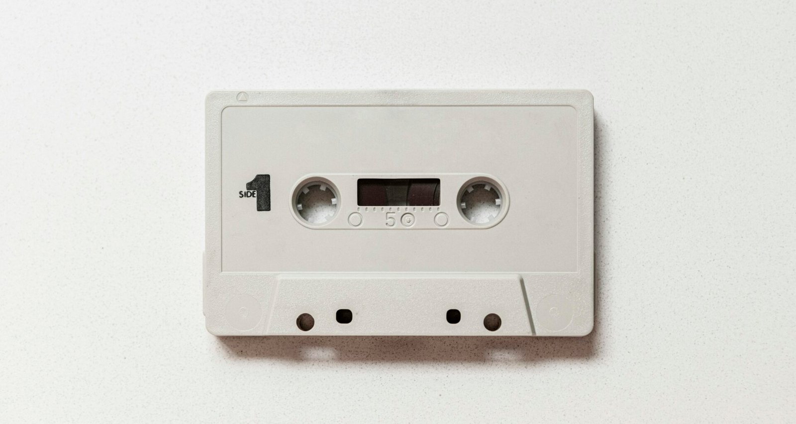 Weiße Audiokassette auf hellem Hintergrund, Fokus auf das Gehäuse und die Spulen, Oldschool-Design als Techniksymbol