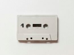 Weiße Audiokassette auf hellem Hintergrund, Fokus auf das Gehäuse und die Spulen, Oldschool-Design als Techniksymbol