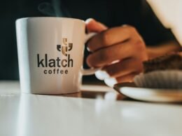 Weiße Keramiktasse auf glattem Holztisch, geeignet für Büro oder Homeoffice, abgebildet aus leichter Vogelperspektive.