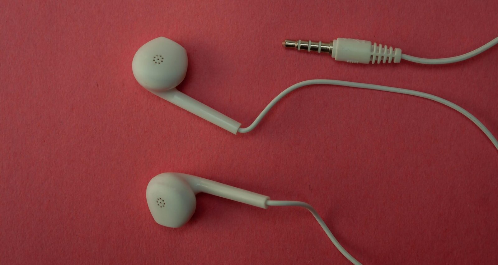 Weiße kabelgebundene Ohrhörer liegen ordentlich auf einer rosa Fläche, Detailaufnahme der Technik-Komponenten.