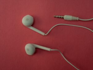 Weiße kabelgebundene Ohrhörer liegen ordentlich auf einer rosa Fläche, Detailaufnahme der Technik-Komponenten.