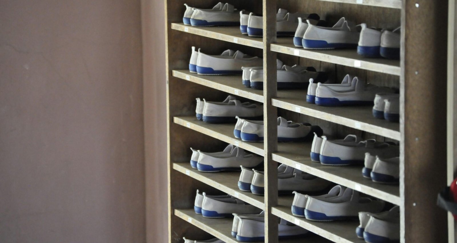 Ein Regal mit weißen und blauen Schuhen steht in einem hellen Zimmer. Die Schuhe sind ordentlich nebeneinander aufgereiht.