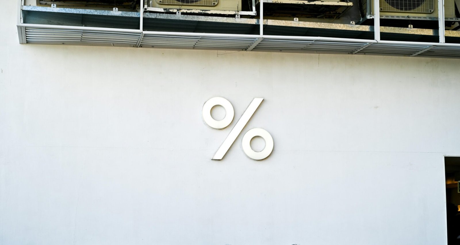 Großes Prozentzeichen-Logo auf einer weißen Wand, fotografiert als modernes Gestaltungselement für Marketing-Visuals.