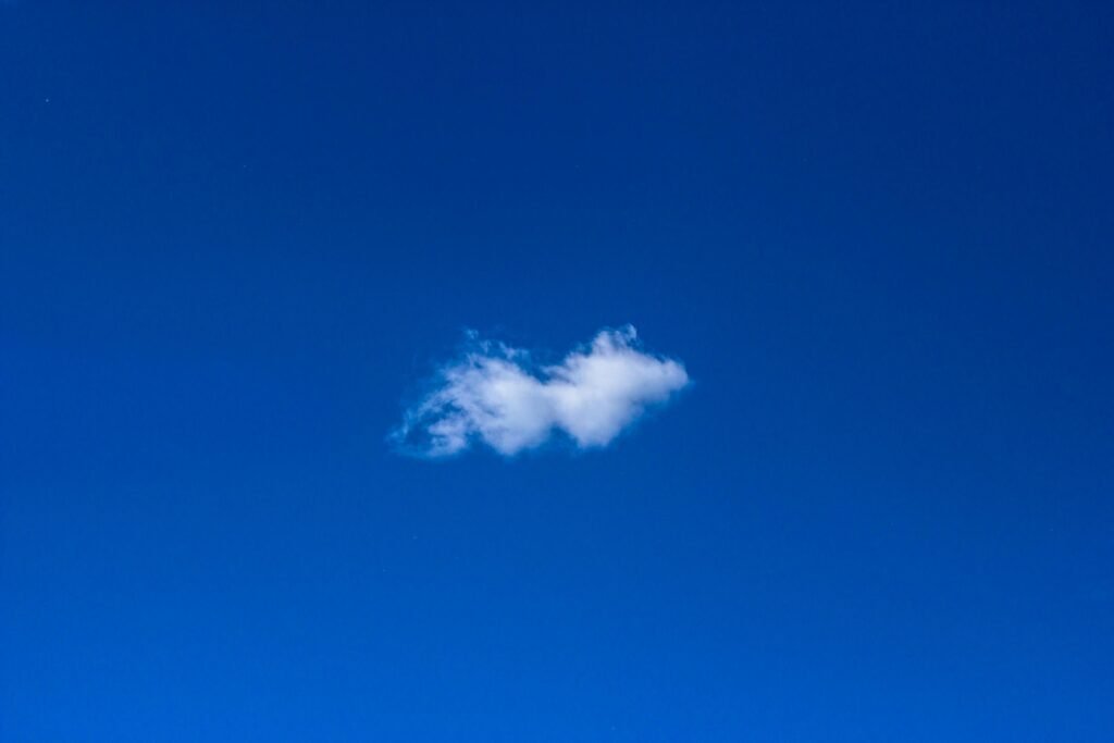 Weiße Wolke am blauen Himmel, minimalistische Darstellung der Natur und Weite des Himmels ohne weitere Elemente.