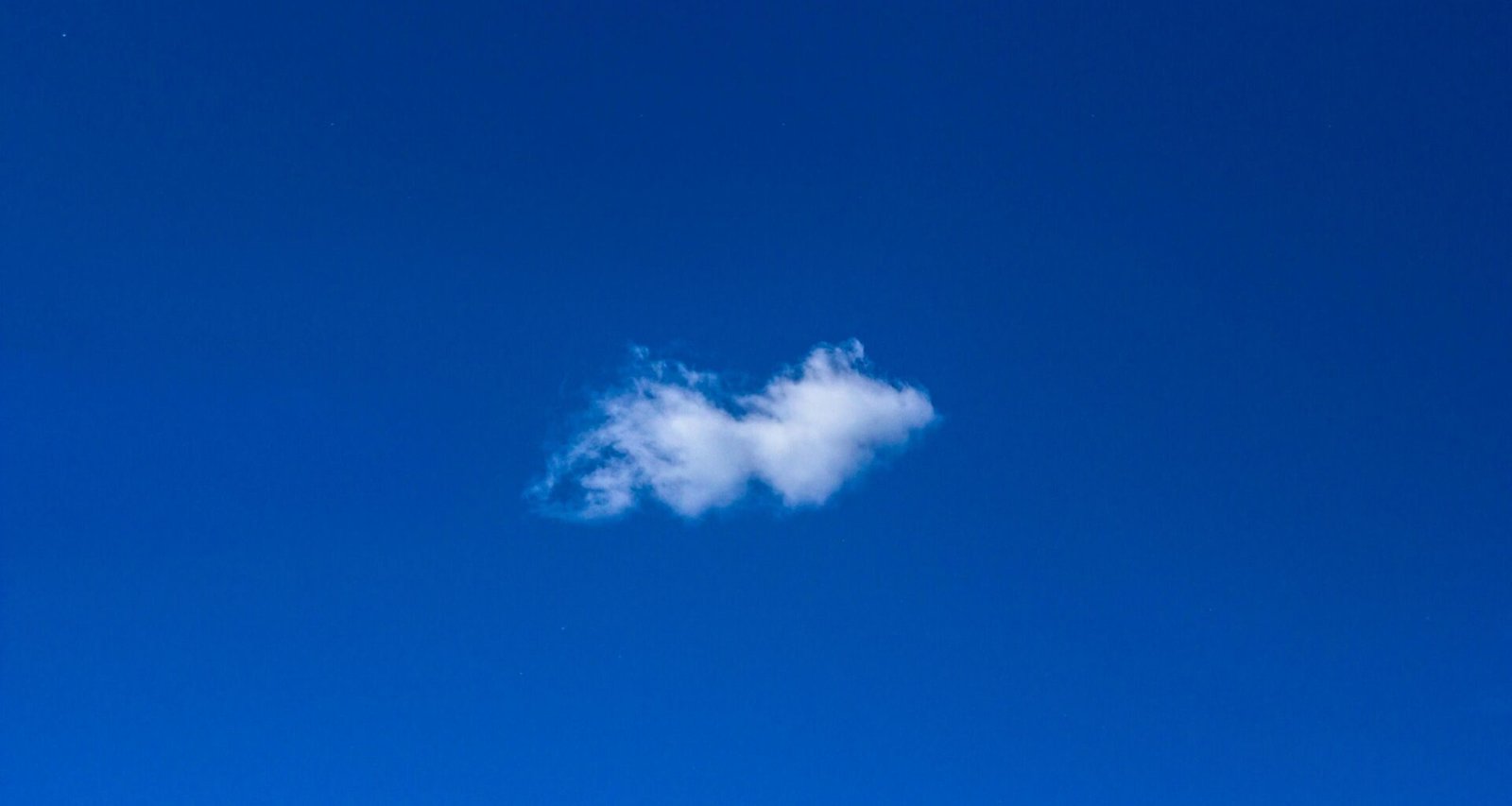 Weiße Wolke am blauen Himmel, minimalistische Darstellung der Natur und Weite des Himmels ohne weitere Elemente.