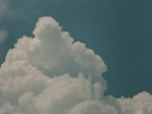 Weiße Wolken ziehen tagsüber über einen blauen Himmel, weiches Licht sorgt für klare Sicht und dezente Strukturen.