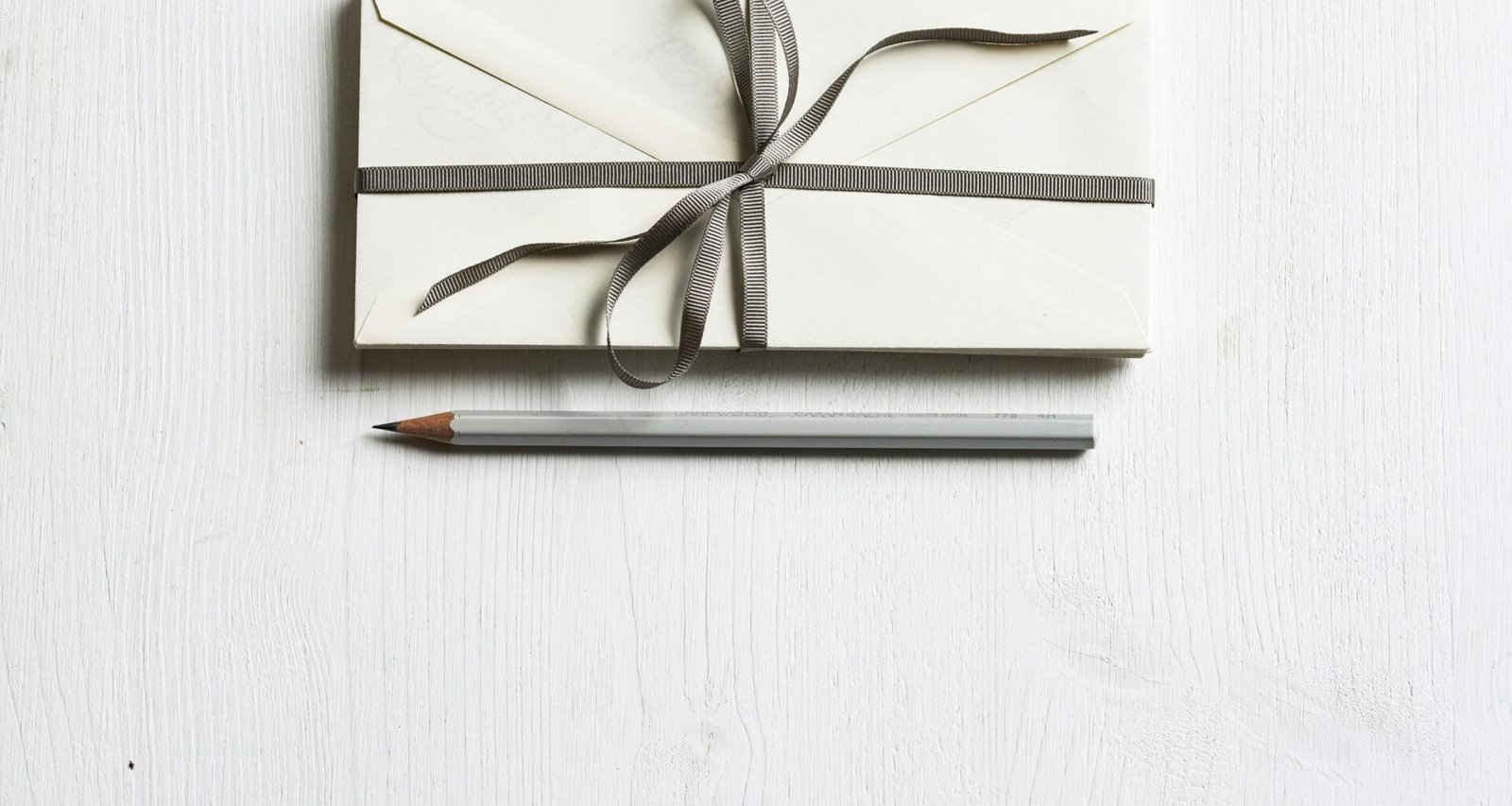 Weißer Umschlag und grauer Bleistift liegen auf einer weißen Fläche nebeneinander – minimalistisches Arrangement für Bürothemen