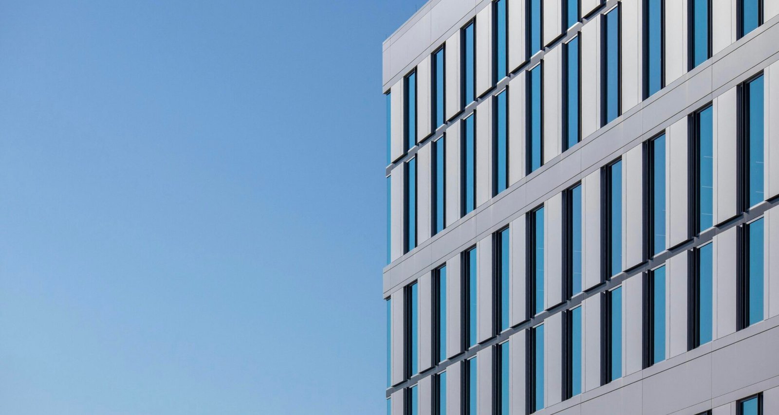 Weißes Betongebäude mit minimalistischer Fassade vor klarem blauen Himmel bei Tageslicht