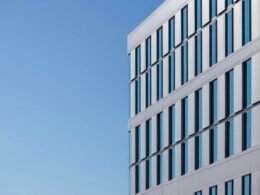 Weißes Betongebäude mit minimalistischer Fassade vor klarem blauen Himmel bei Tageslicht