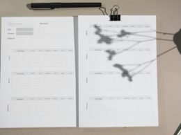 Ein Stapel weißer Druckerpapiere liegt ordentlich auf einem braunen Holztisch, bereit zum Einsatz im Büroalltag.