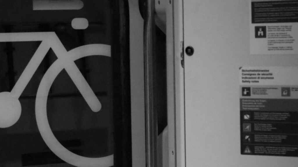 Weißes Fahrradsymbol auf dunklem Boden, platziert neben einer weißen Tür, fotografiert aus der Vogelperspektive.