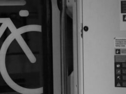 Weißes Fahrradsymbol auf dunklem Boden, platziert neben einer weißen Tür, fotografiert aus der Vogelperspektive.