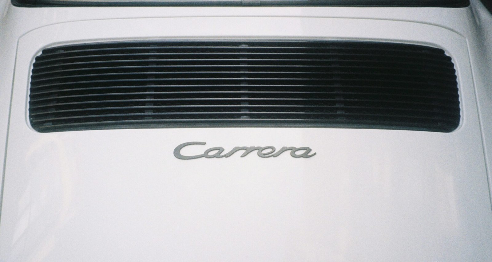 Rückansicht eines weißen Autos mit dem Schriftzug Carrera am Heck, Detailperspektive auf Fahrzeugemblem