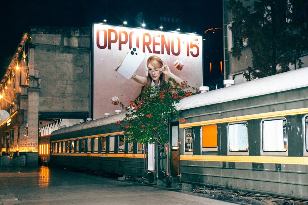 Leuchtende Billboard-Werbung an Zugschienen bei Nacht, vorbeifahrende Züge und beleuchtete Werbetafeln in urbaner Umgebung