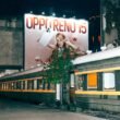 Leuchtende Billboard-Werbung an Zugschienen bei Nacht, vorbeifahrende Züge und beleuchtete Werbetafeln in urbaner Umgebung