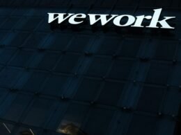 'We Work' Schild an der Fassade eines modernen Bürogebäudes, Symbol für neue Formen der Zusammenarbeit in Unternehmen.