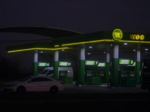 Beleuchtete WOG Tankstelle mit Zapfsäulen und Überdachung in urbaner Umgebung, aufgenommen am Abend
