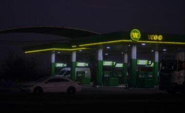 Beleuchtete WOG Tankstelle mit Zapfsäulen und Überdachung in urbaner Umgebung, aufgenommen am Abend