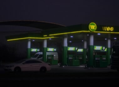 Beleuchtete WOG Tankstelle mit Zapfsäulen und Überdachung in urbaner Umgebung, aufgenommen am Abend