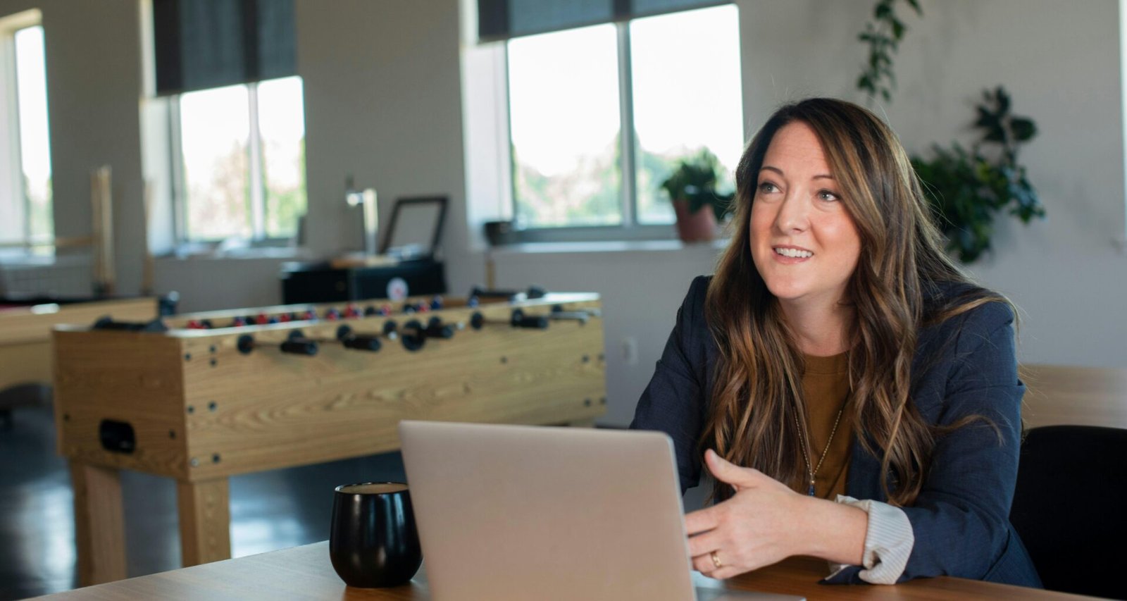 Frau mit brauner Strickjacke arbeitet fokussiert an einem silbernen MacBook Laptop am Schreibtisch