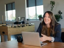 Frau mit brauner Strickjacke arbeitet fokussiert an einem silbernen MacBook Laptop am Schreibtisch