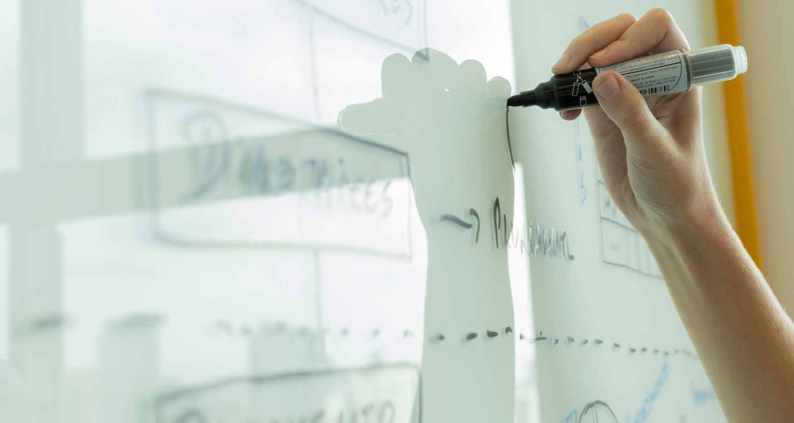 Eine Person zeichnet ein Diagramm auf ein Whiteboard, als Teil eines kreativen Planungsprozesses im Büro.