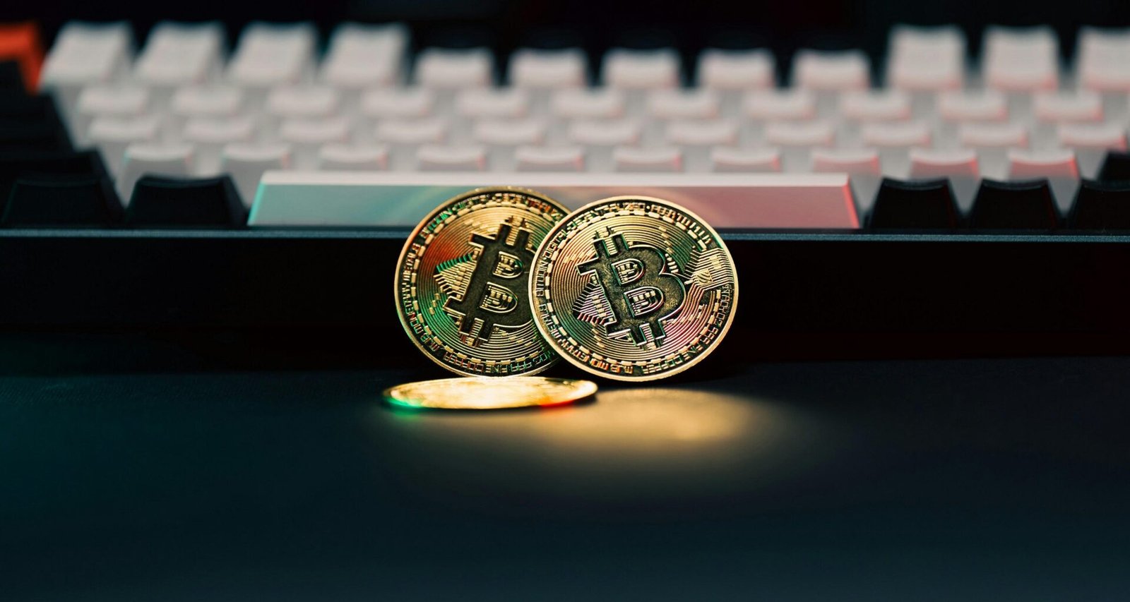 Zwei physische Bitcoin-Münzen liegen neben einer weißen Computertastatur auf einem Schreibtisch.