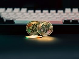 Zwei physische Bitcoin-Münzen liegen neben einer weißen Computertastatur auf einem Schreibtisch.