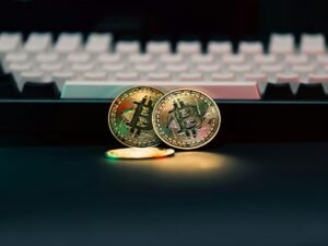 Zwei physische Bitcoin-Münzen liegen neben einer schwarzen Computer-Tastatur auf einem Schreibtisch.