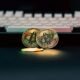 Zwei physische Bitcoin-Münzen liegen neben einer weißen Computertastatur auf einem Schreibtisch.