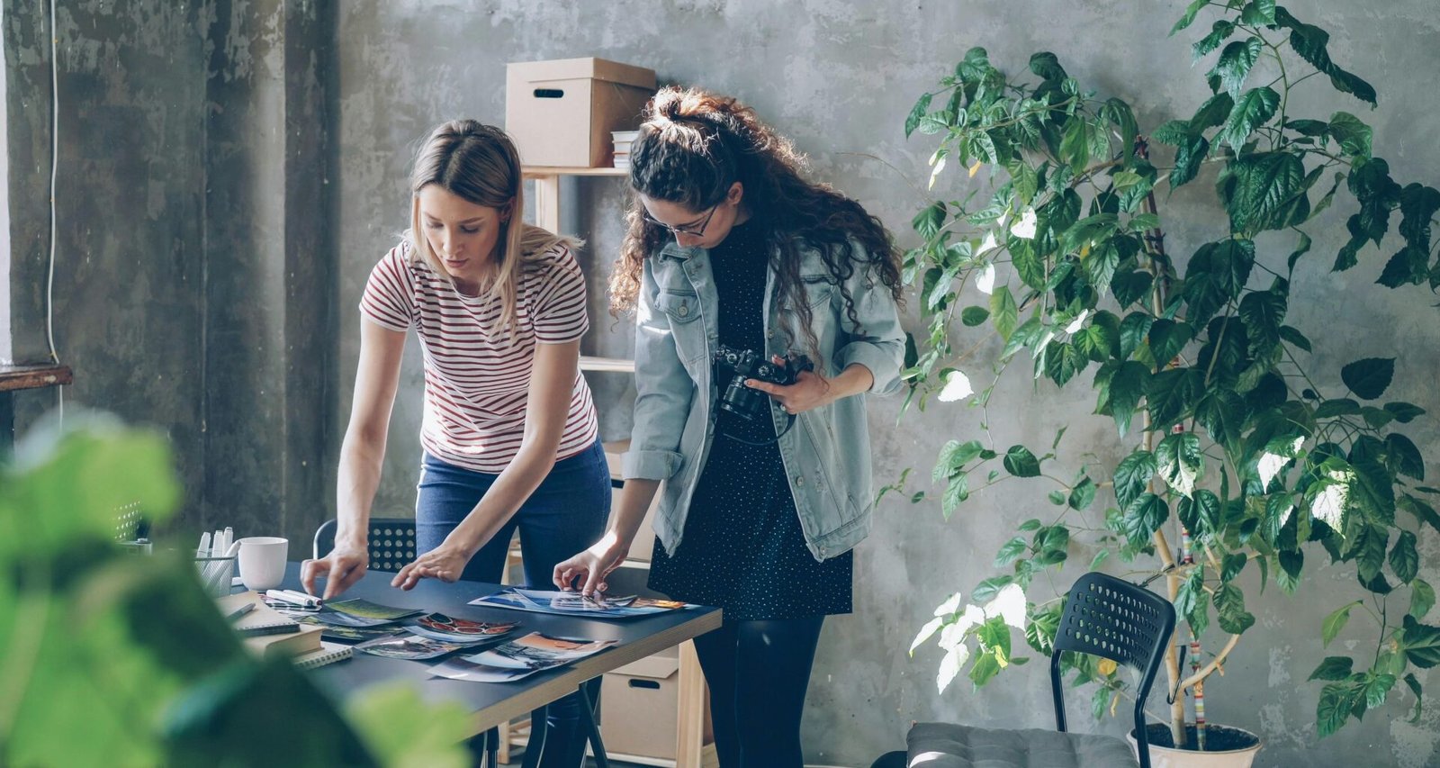 Zwei Frauen sitzen an einem Tisch und arbeiten gemeinsam an Dokumenten in einem modernen Büro