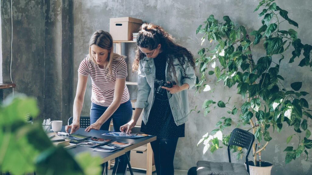 Zwei Frauen sitzen an einem Tisch, diskutieren und arbeiten gemeinsam an Unterlagen in einem modernen Büro