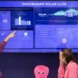 Zwei Frauen schauen sich gemeinsam die Anzeige eines Solarclub-Dashboards an und diskutieren die dort gezeigten Daten.