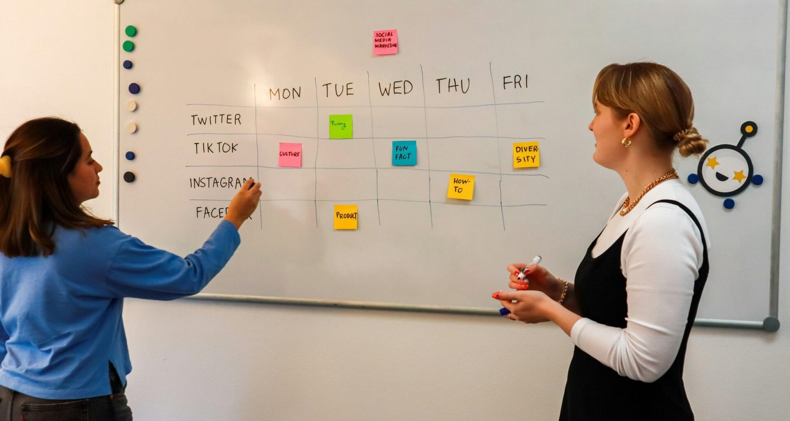 Zwei Frauen diskutieren vor einem Whiteboard mit bunten Klebezetteln in einem modernen Büro.