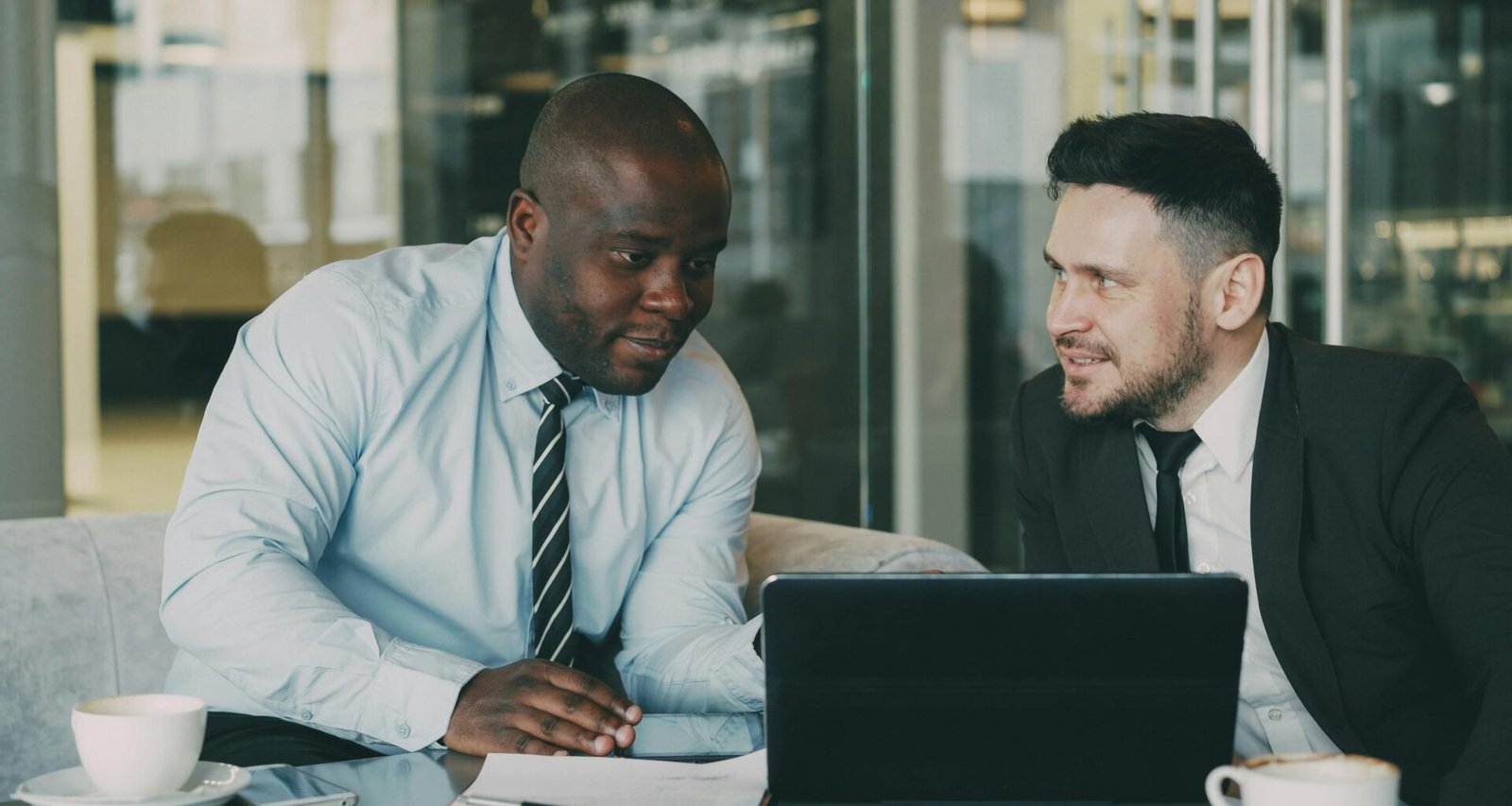 Zwei Firmenangehörige sitzen an einem Tisch und besprechen diverse Dokumente zur gemeinsamen Auswertung.