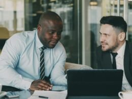 Zwei Firmenangehörige sitzen an einem Tisch und besprechen diverse Dokumente zur gemeinsamen Auswertung.