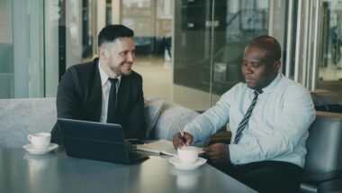 Zwei Geschäftsleute sitzen in einem Café und besprechen gemeinsam Dokumente bei einer Tasse Kaffee.